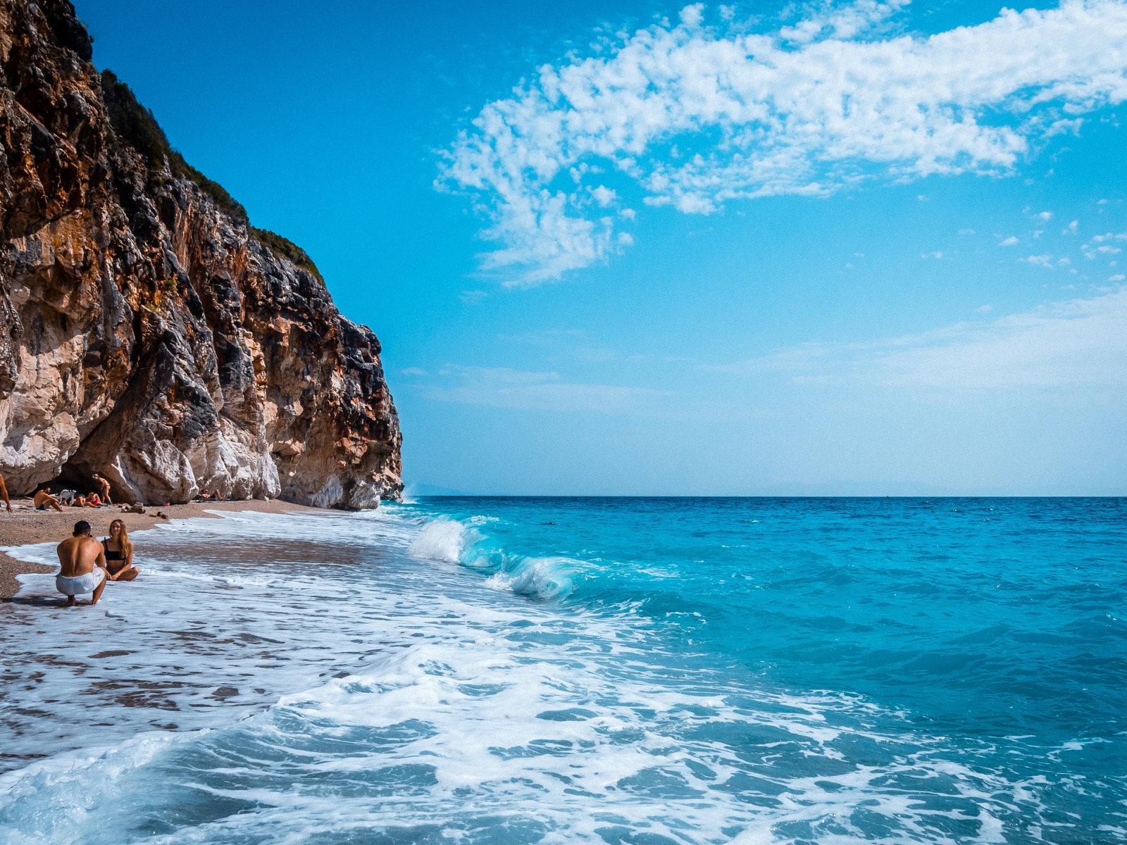 Couple sitting on Gjipe Beach with dramatic cliffs and turquoise waves