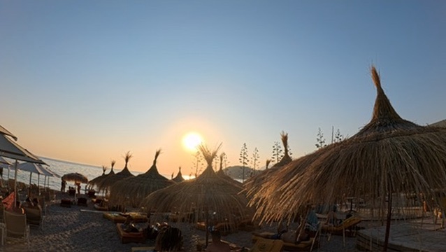Sunset glow through straw beach umbrellas and sunbeds on the Albanian Riviera coast